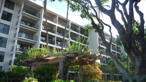 A multi-story hotel with balconies, lush greenery, and a pergola with flowers.