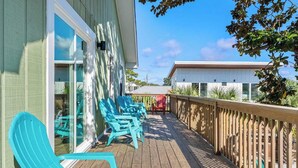 A wooden deck with turquoise chairs, a wooden railing, and a building with large windows.