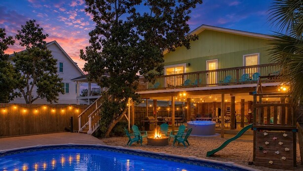A swimming pool with a wooden deck, outdoor seating, a hot tub, and a covered patio area.