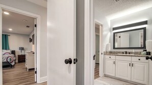 A hotel room with a bed, a nightstand, a dresser, and a bathroom with a sink and mirror.