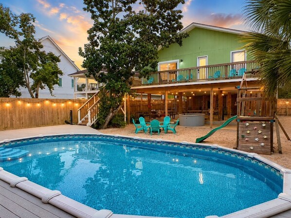 Une piscine avec une terrasse en bois, un patio couvert doté de meubles d’extérieur et un toboggan.