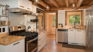 A modern kitchen with stainless steel appliances, wooden flooring, and a large window providing natural light.
