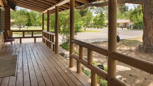 A wooden deck with a railing, benches, and a view of a park with trees and a building in the background.