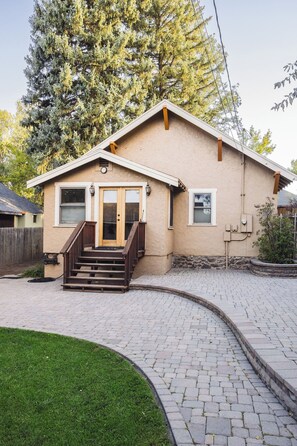 A single-story house with a front porch, a wooden staircase, and a paved driveway.