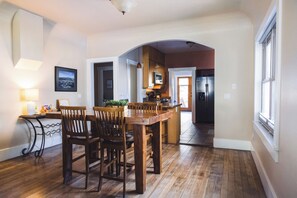 Une cuisine spacieuse avec un plancher en bois, un coin repas avec une grande table et des chaises, et une vue sur une autre pièce accessible par une arche.
