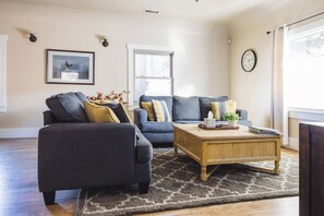 A living room with two sofas, a coffee table, a rug, a framed picture, a window, and a wall clock. - Downtown Flagstaff Bungalow - 5 minute walk to downtown (Flagstaff)