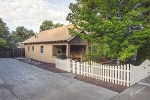 Een gelijkvloers huis met een veranda, een hek van planken en een verharde oprit.