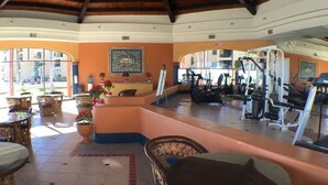 Ein Fitnessraum mit Trainingsgeräten, Korbmöbeln und gefliestem Boden.