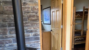 A room with a black wood-burning stove, wooden flooring, a stone wall, and a wooden door leading to another room. - Summer is coming!   (Longville)