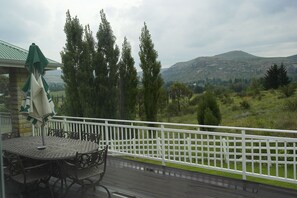 A deck with a table and chairs, a white fence, and a view of a hilly landscape with trees and a mountain. - Fairways (Clarens)