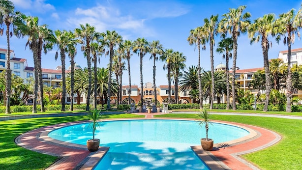 A swimming pool surrounded by palm trees and a building with a dome. - Capri 101 (Cape Town)