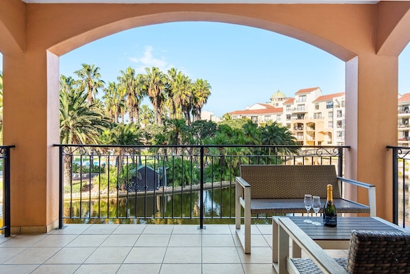 Un balcon avec vue sur une étendue d’eau, des palmiers et des bâtiments en arrière-plan.