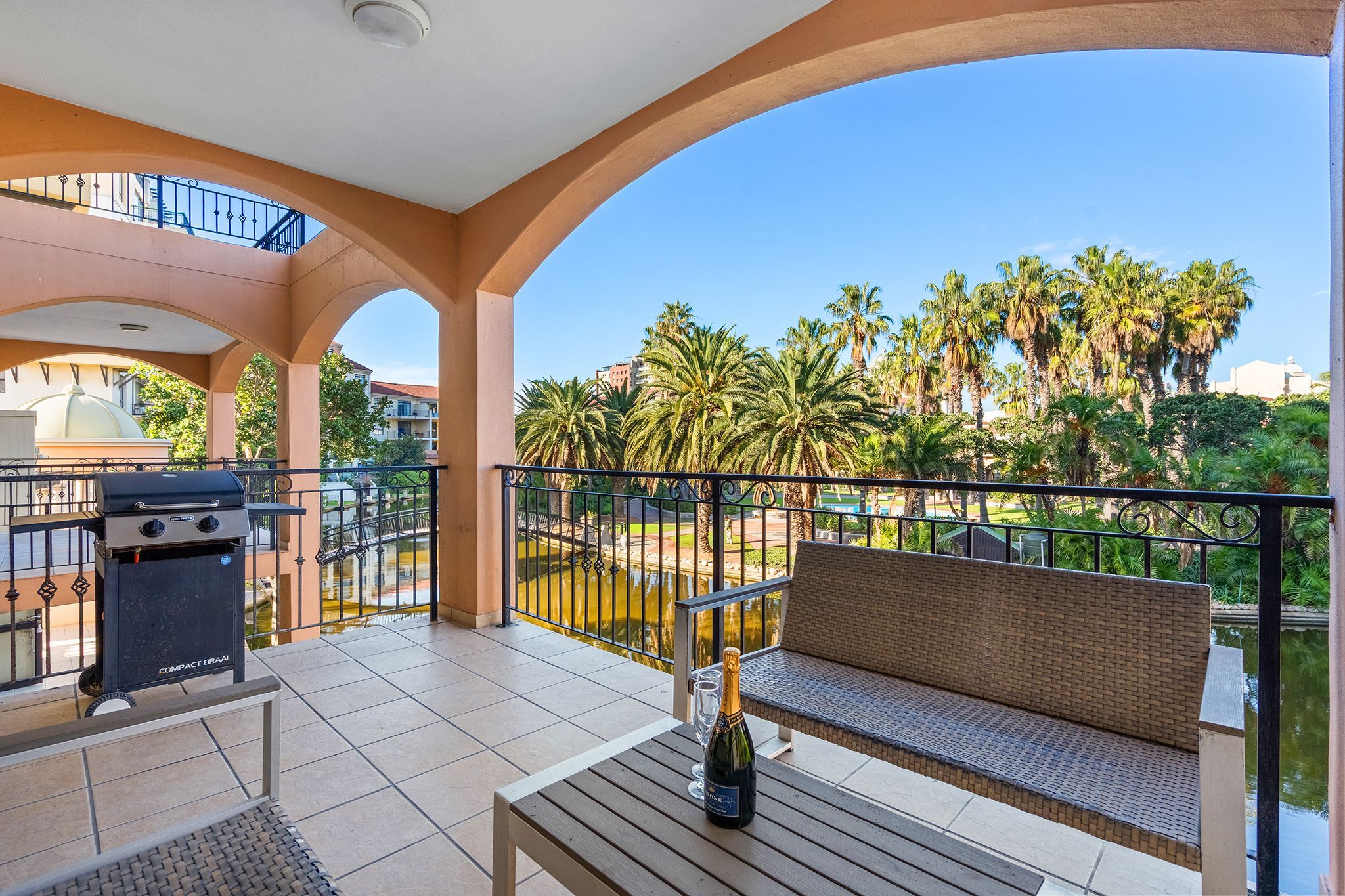 A balcony with a grill, a bottle of champagne, and a bench.