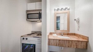 A compact kitchen with a microwave, stove, and oven. A bathroom with a sink and mirror is also visible. - Studio 6 Corpus Christi, TX - North (Corpus Christi)