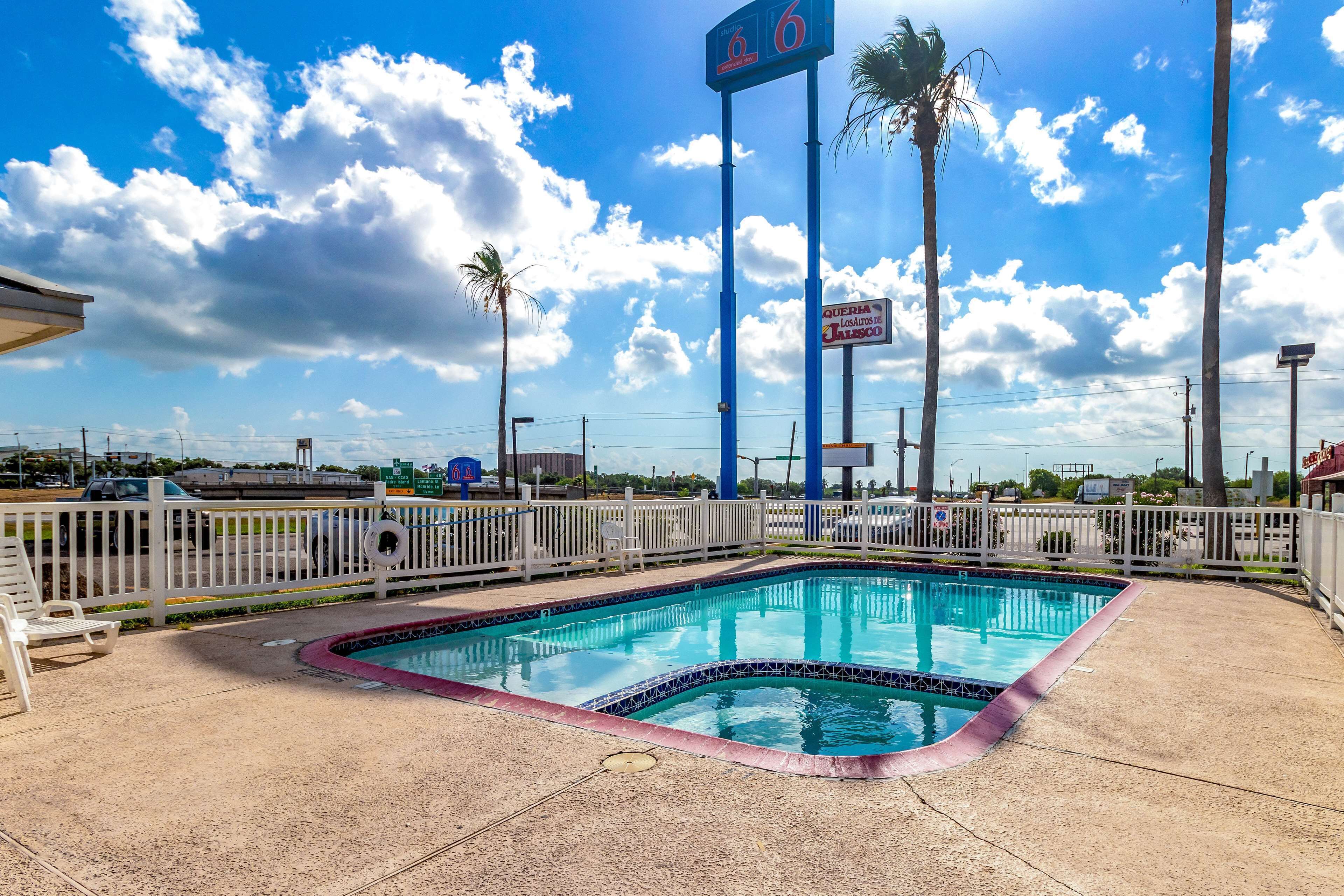 A swimming pool with a blue sign above it, surrounded by a white fence and palm trees.