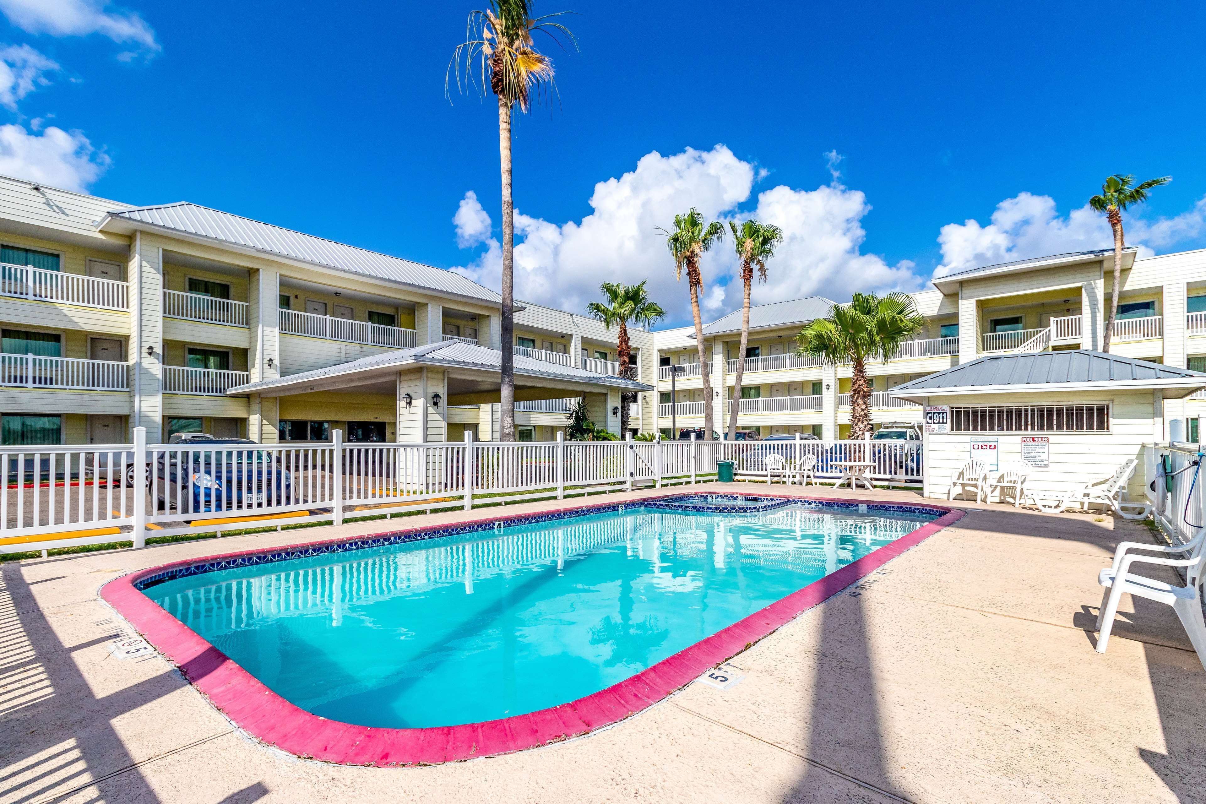 A hotel with a swimming pool, white balconies, and palm trees.