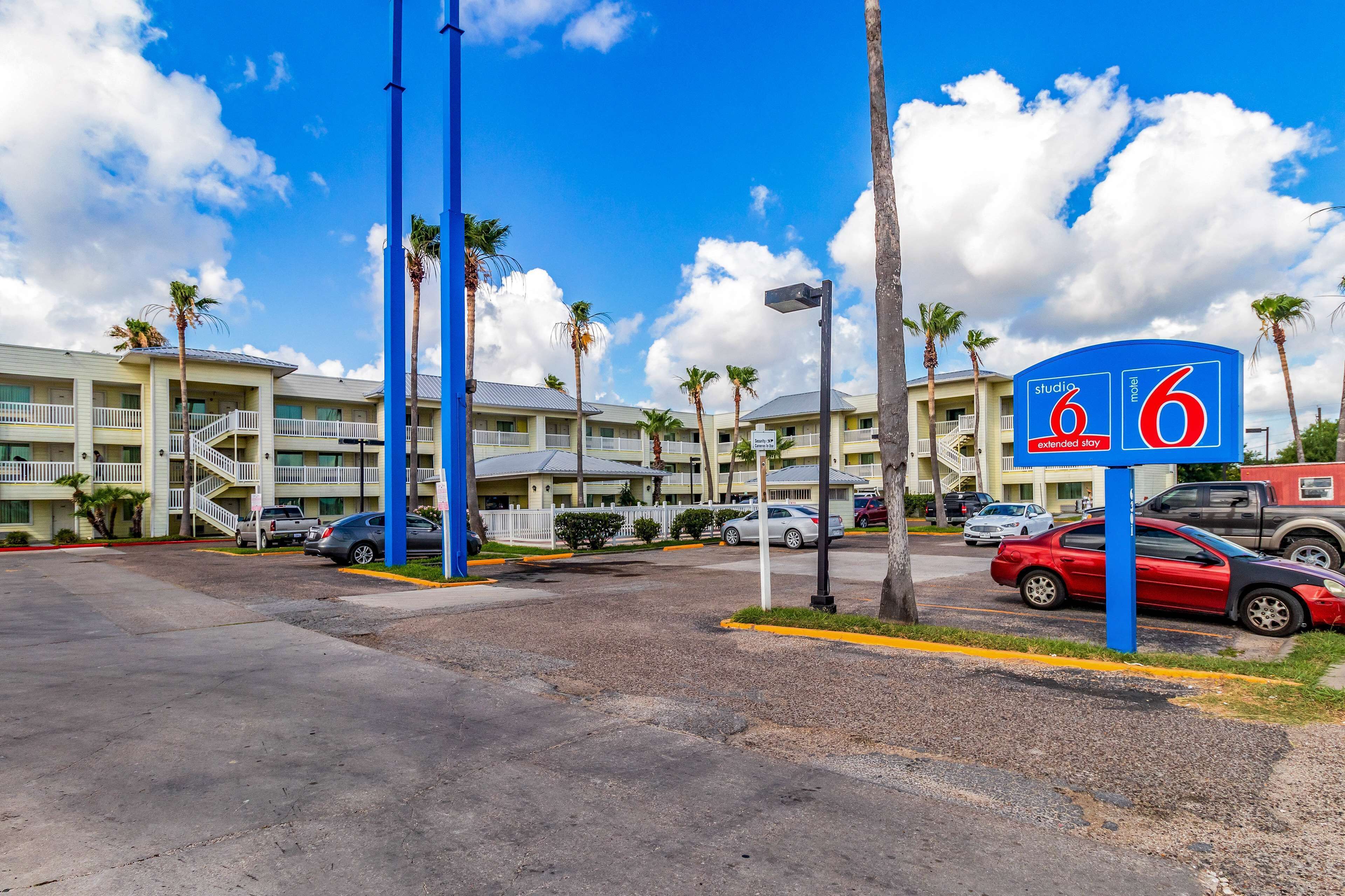 A motel with a sign indicating '6 extended stay' rooms, surrounded by palm trees and parked cars.