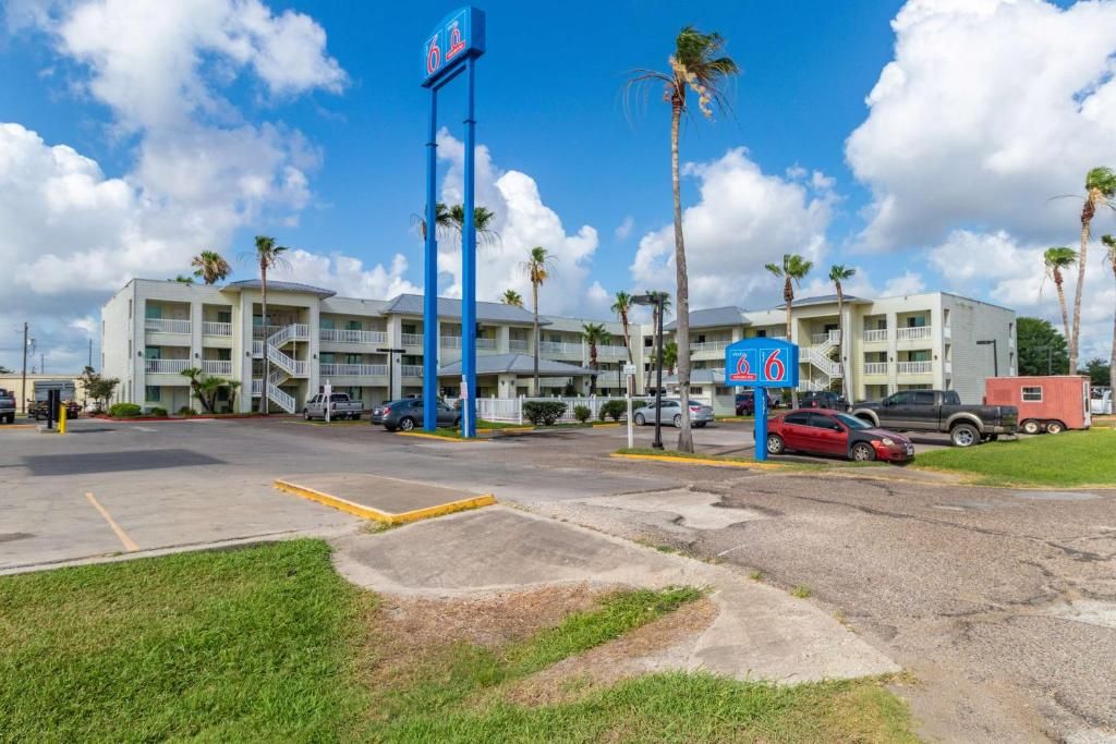 A hotel with a parking lot, multiple floors, and palm trees.