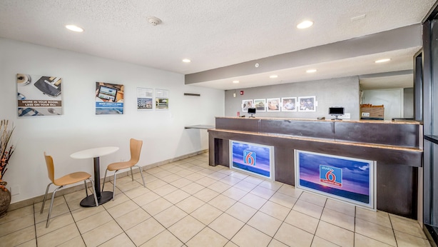 A reception area with a reception desk, two chairs, a small table, and a tiled floor. - Studio 6 Corpus Christi, TX - North (Corpus Christi)
