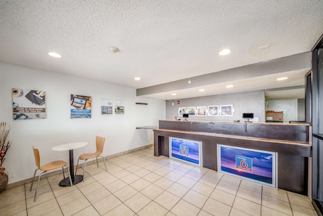 A reception area with a reception desk, two chairs, a small table, and a tiled floor.