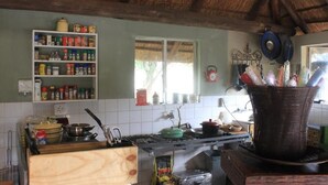 A kitchen with a thatched roof, a stove, a sink, and a variety of cooking utensils and containers. - Grootgeluk Bush Camp (Mookgopong)