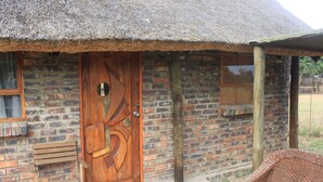 A rustic building with a thatched roof, a wooden door with a circular window, and a brick wall. - Grootgeluk Bush Camp (Mookgopong)