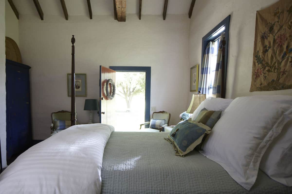 A bedroom with a large bed, a chair, a lamp, and a door leading to an outdoor area.