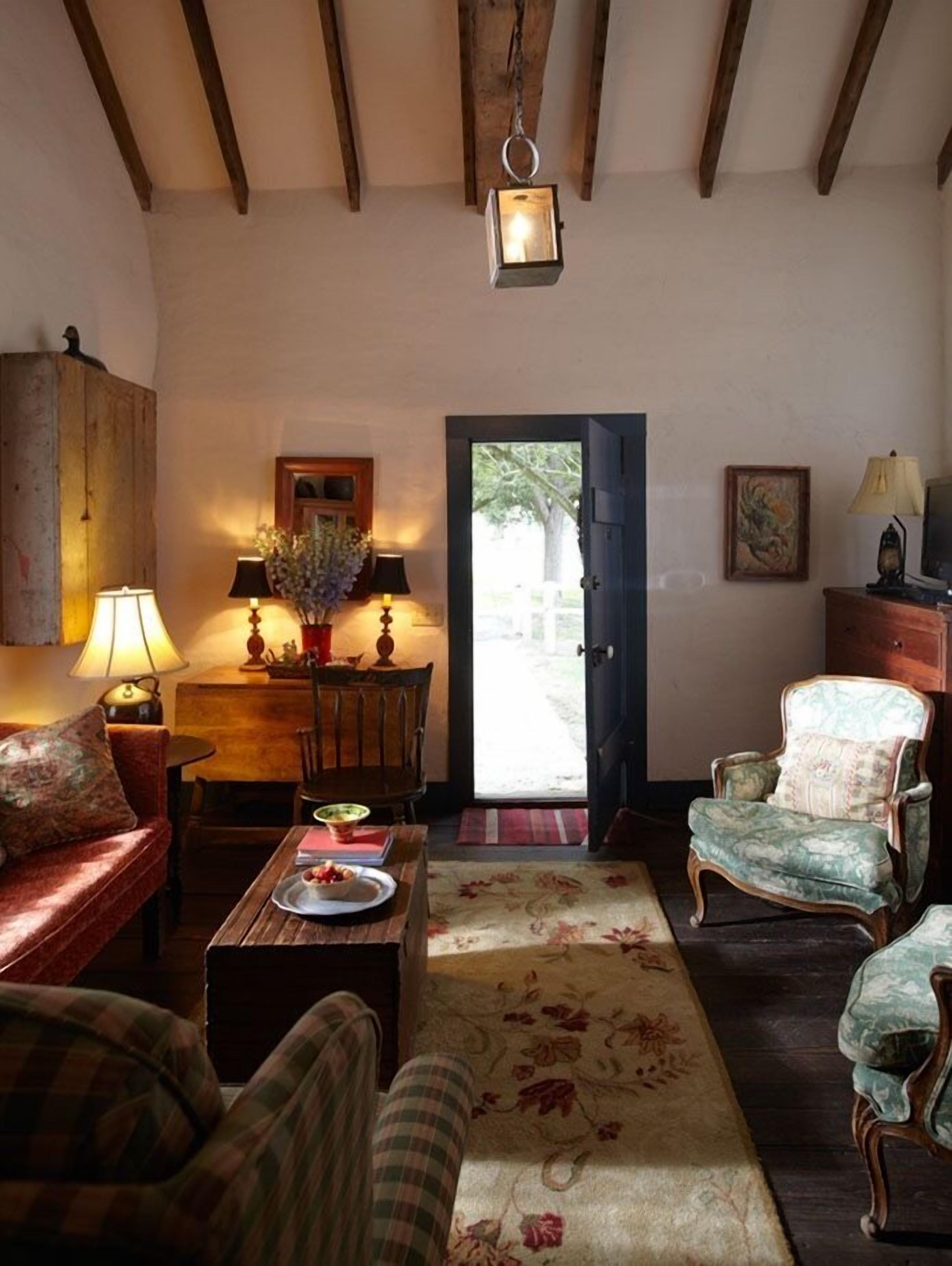 Una sala de estar acogedora con techo de madera, una mesa de comedor con sillas, un sofá, un tapete estampado y una puerta que da al exterior.