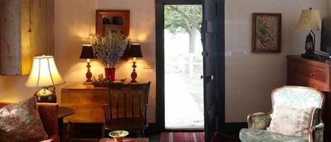 Una sala de estar acogedora con techo de madera, una mesa de comedor con sillas, un sofá, un tapete estampado y una puerta que da al exterior.
