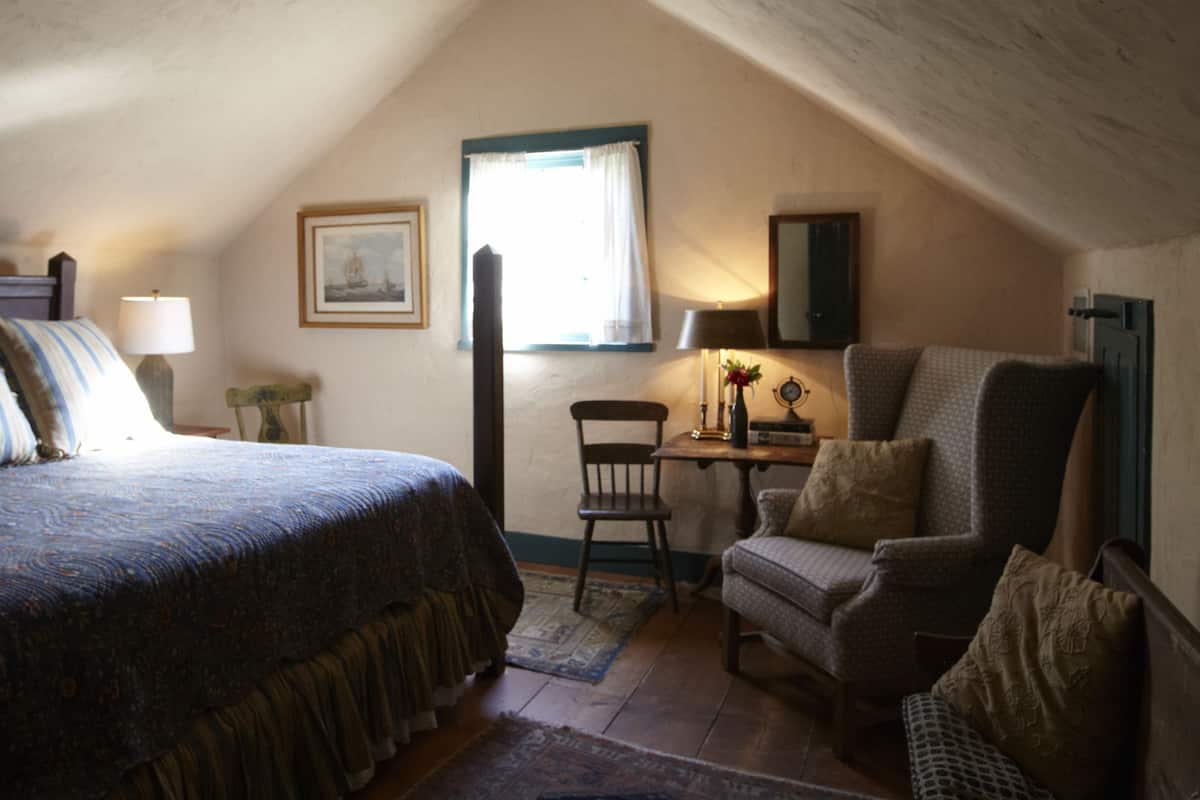 A cozy attic bedroom with a sloped ceiling, a large bed, a desk, and a chair.