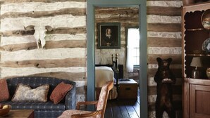 A rustic log cabin interior with a wooden ceiling, a chandelier, a sofa, a chair, a bear statue, and a mirror. - Settlers Crossing (Fredericksburg)