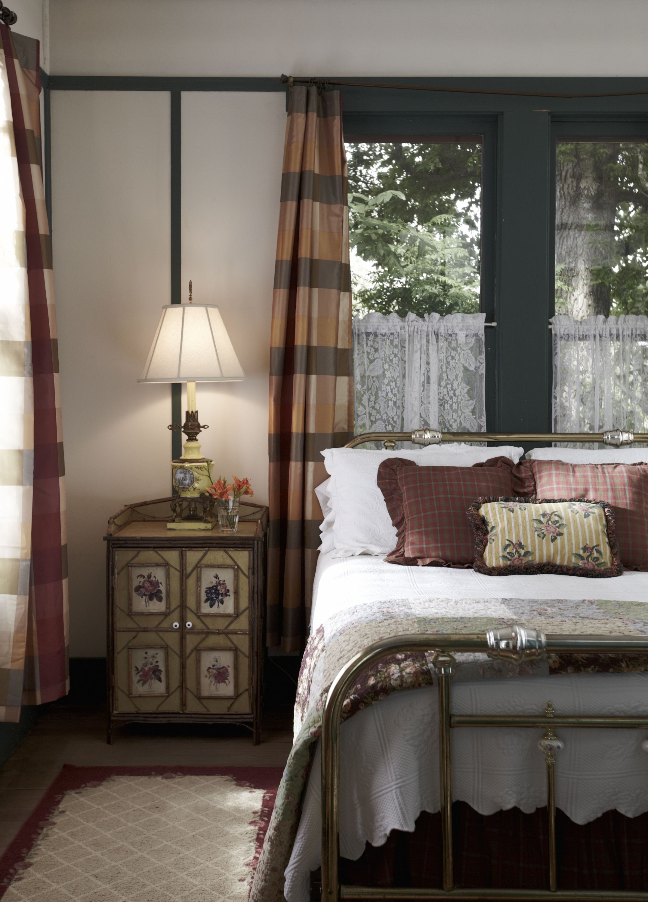 Un dormitorio con cama, mesita de noche con lámpara, cómoda con motivos florales y ventana con cortinas.