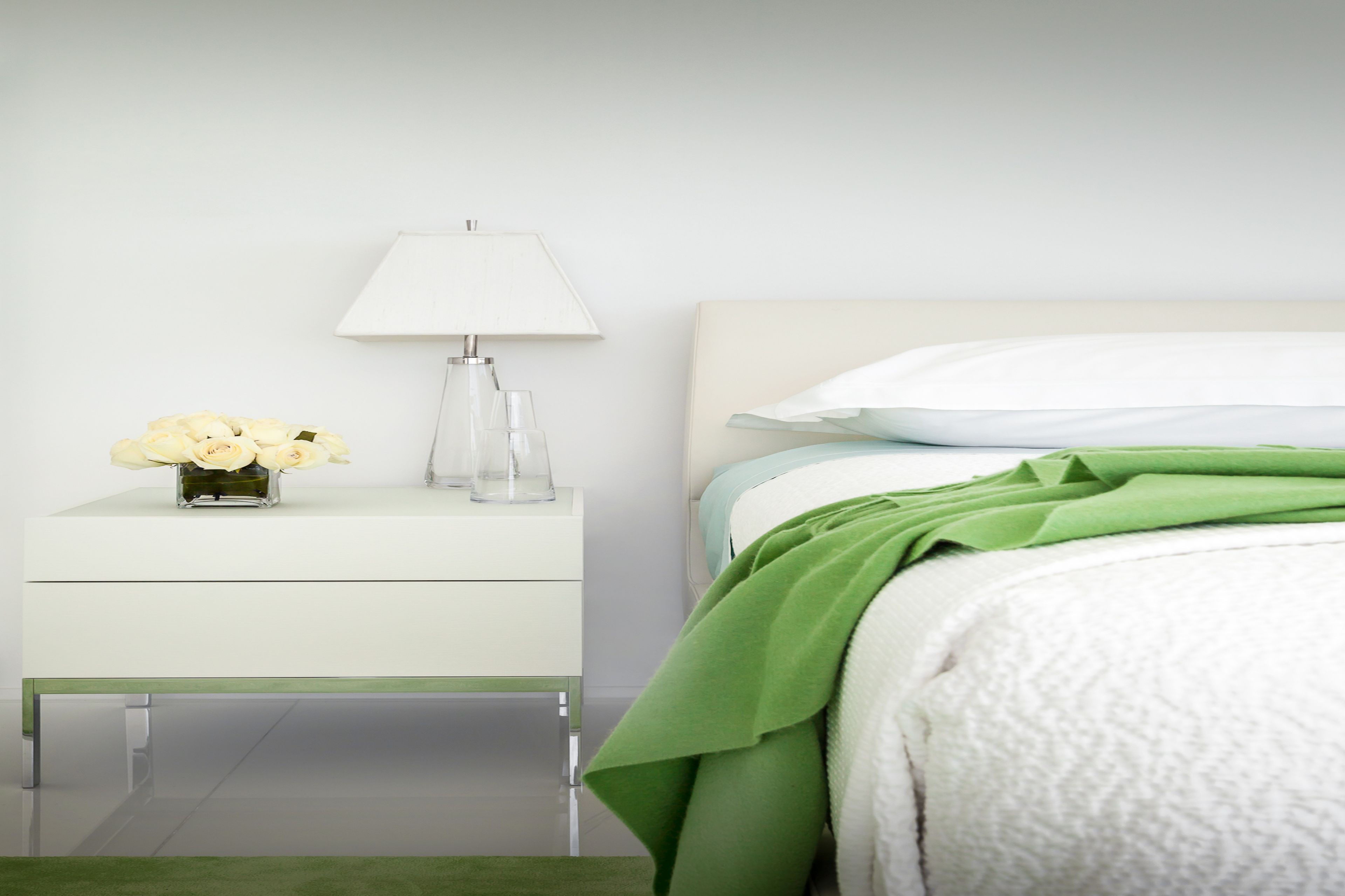 A neatly arranged bedroom with a bed, a bedside table with a lamp, and a vase of flowers.