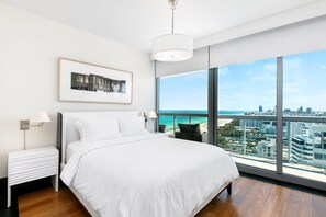 A modern bedroom with a large bed, a nightstand, a framed picture, and a view of the city and ocean. - Setai Residences by Flashstay (Miami Beach)