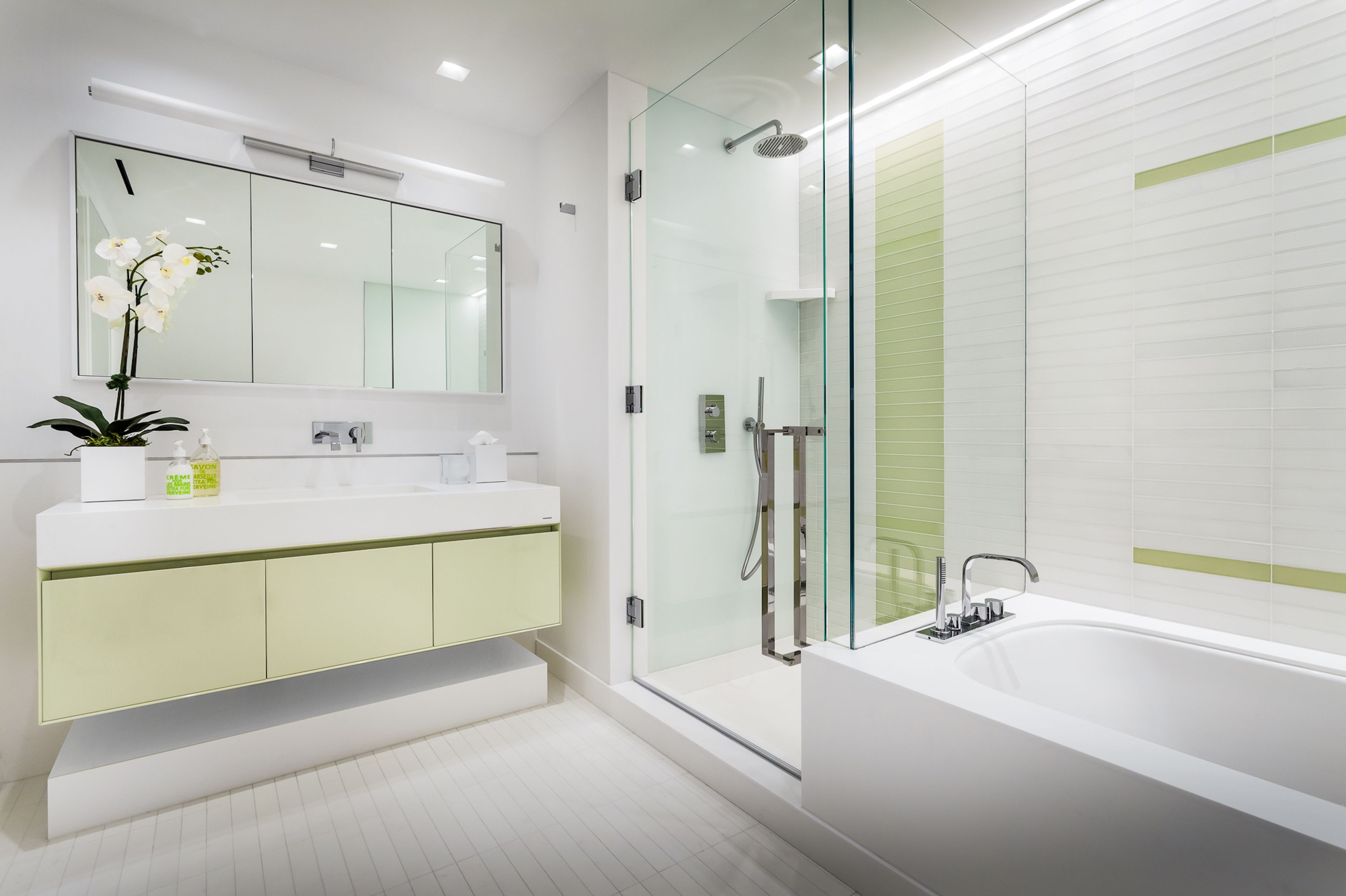 A modern bathroom with a glass-enclosed shower, a large mirror, and a white sink with a green cabinet.