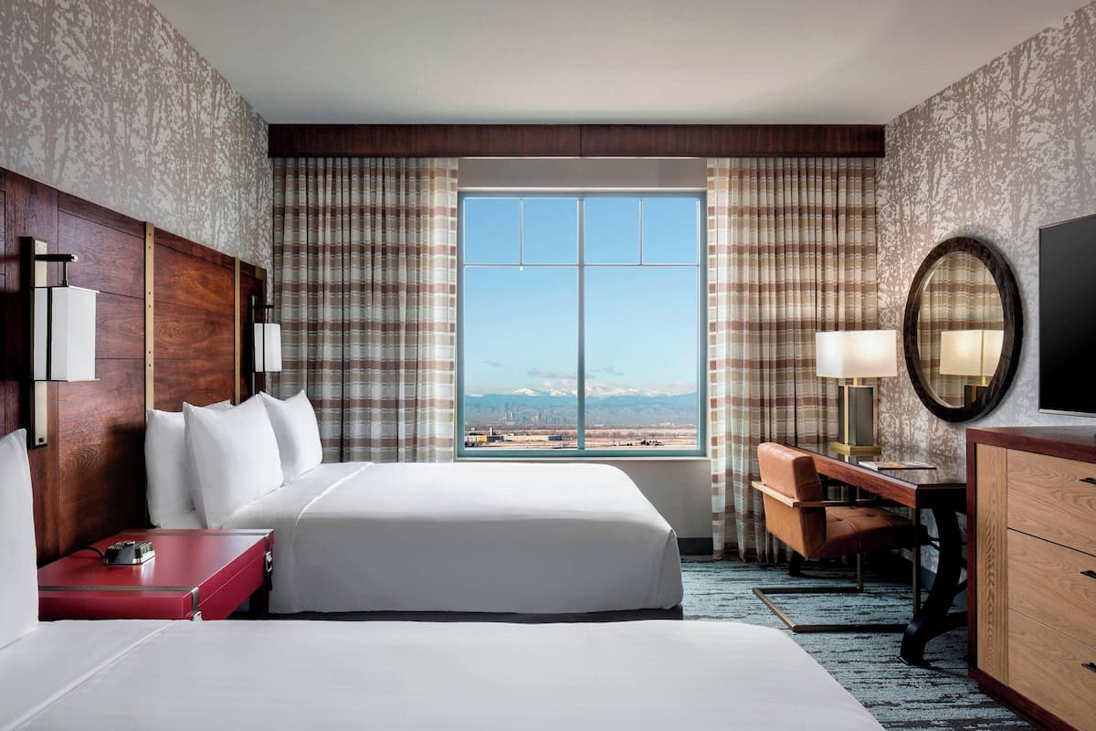 A hotel room with a large bed, a desk, a chair, a TV, and a view of mountains through the window.