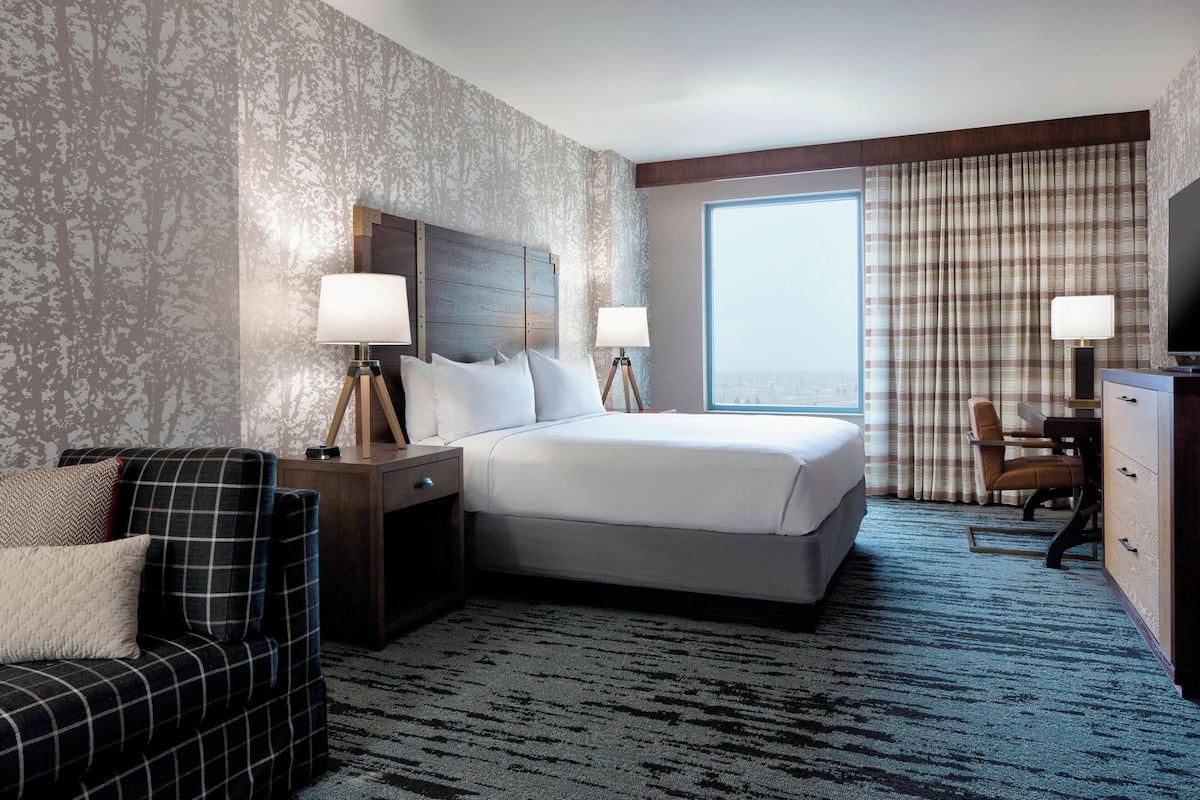 A hotel room with a large bed, two bedside tables with lamps, a sofa, a desk with a chair, and a TV.