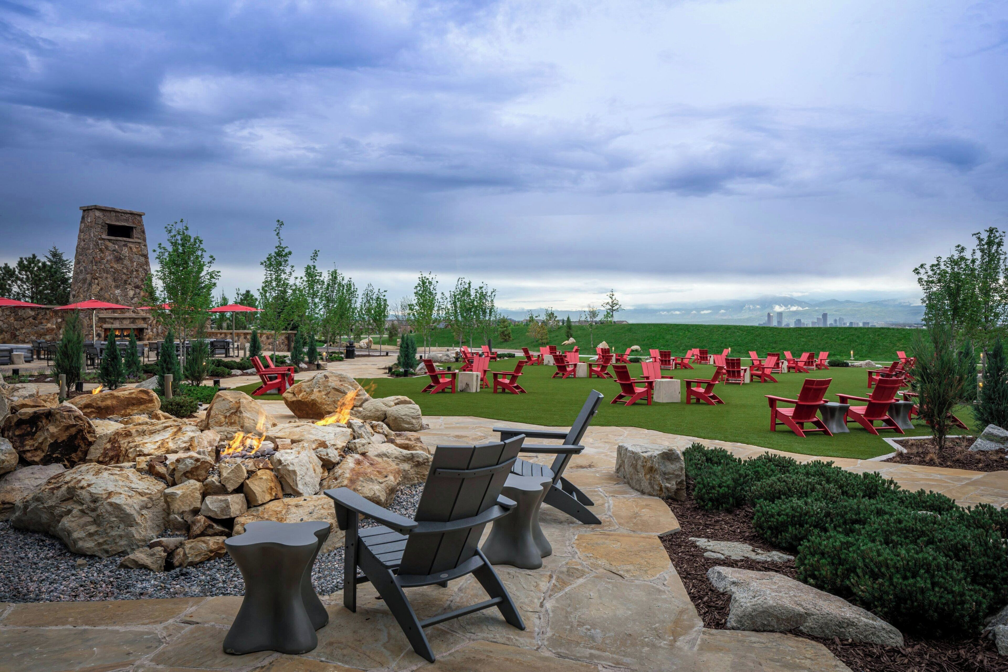 Une terrasse extérieure avec des sièges en pierre, un foyer et des chaises rouges.