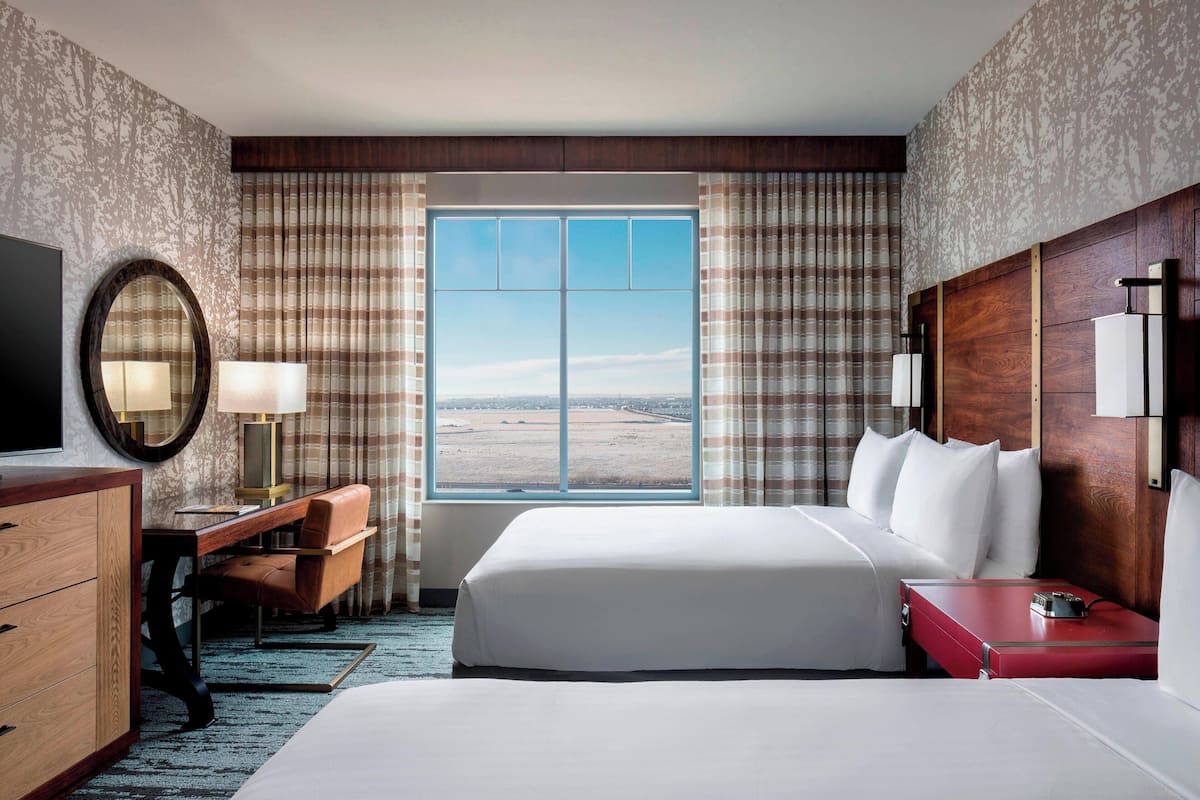 A hotel room with a large bed, a desk with a chair, a TV, and a view of the landscape through the window.