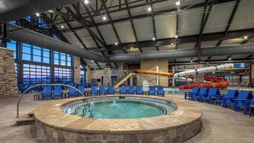 Une piscine intérieure avec un jacuzzi, des chaises bleues et un toboggan aquatique.