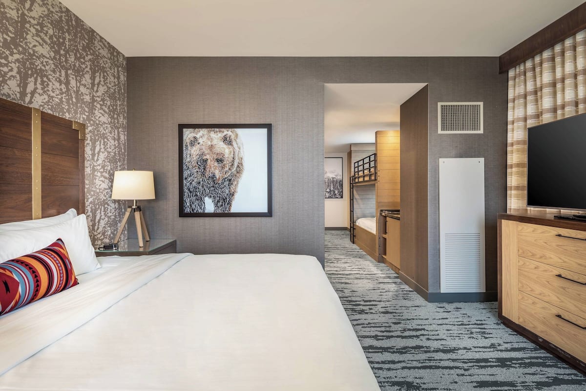 A hotel room with a large bed, a television, a desk with a lamp, a framed picture on the wall, and a wardrobe.