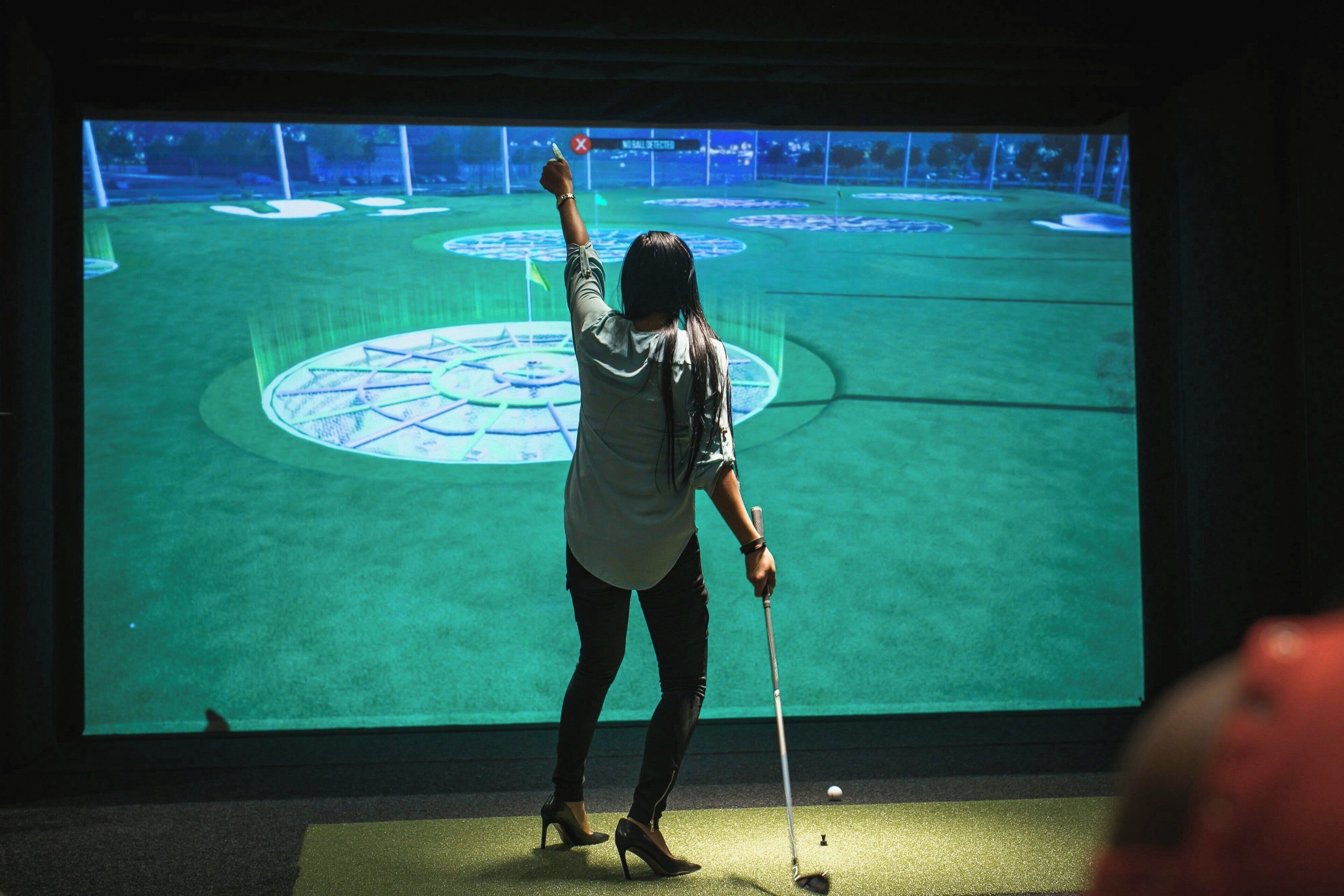 A person playing golf in a dimly lit indoor setting with a large screen displaying a golf course.