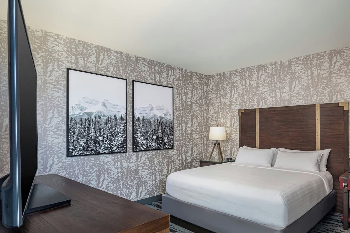 A hotel room with a bed, a desk, a TV, and two framed pictures on the wall.