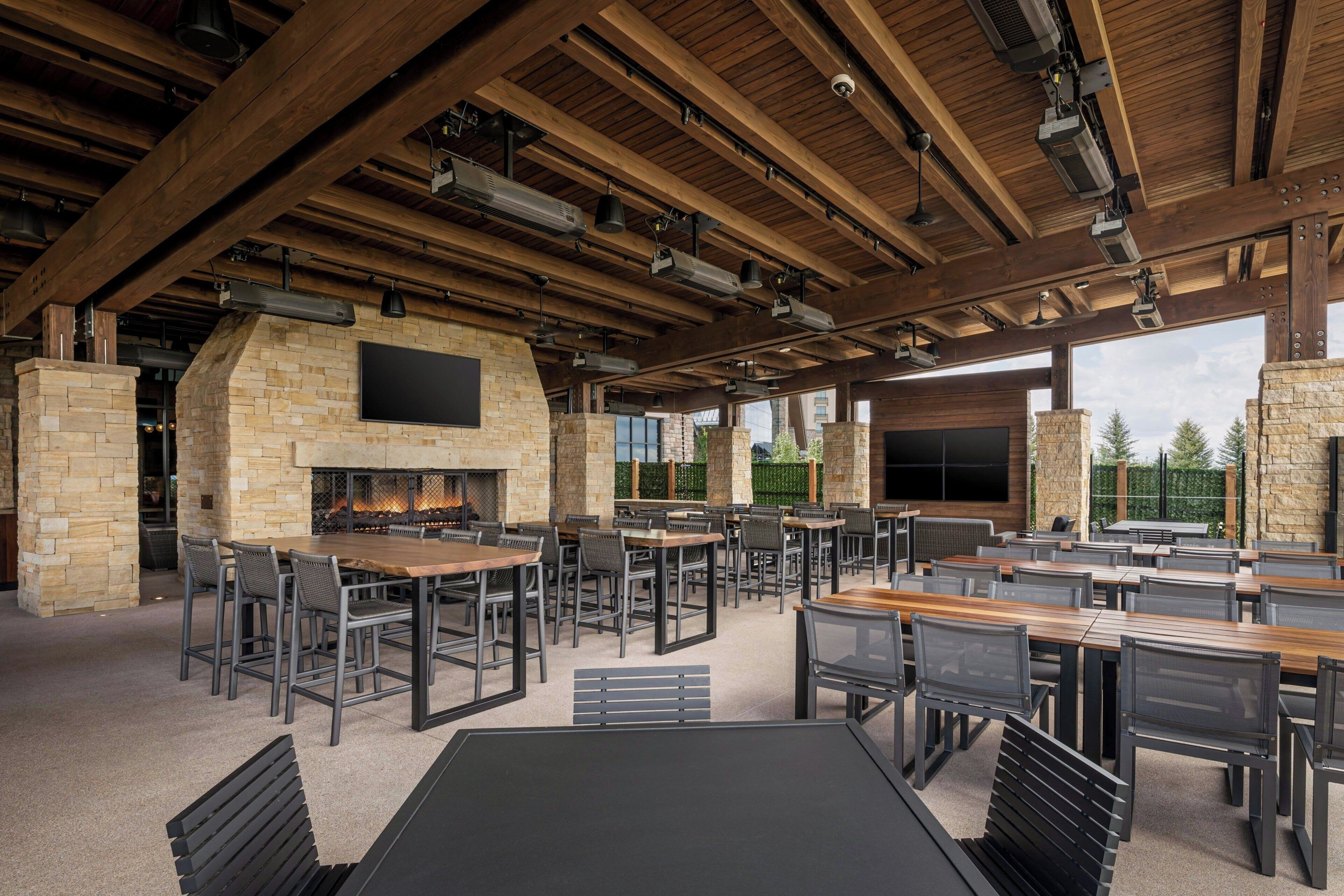 An outdoor dining area with stone walls, wooden beams, and multiple tables and chairs.