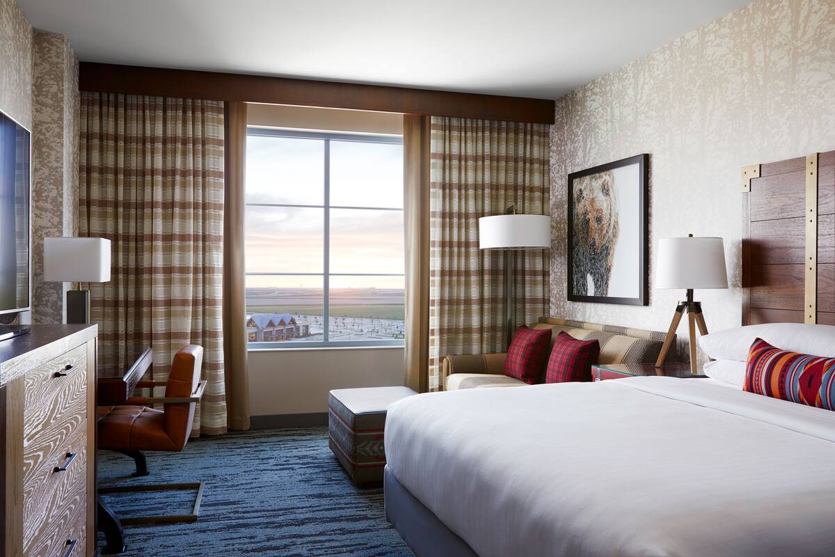 A hotel room with a large bed, a desk with a chair, a sofa, a TV, and a window with curtains.