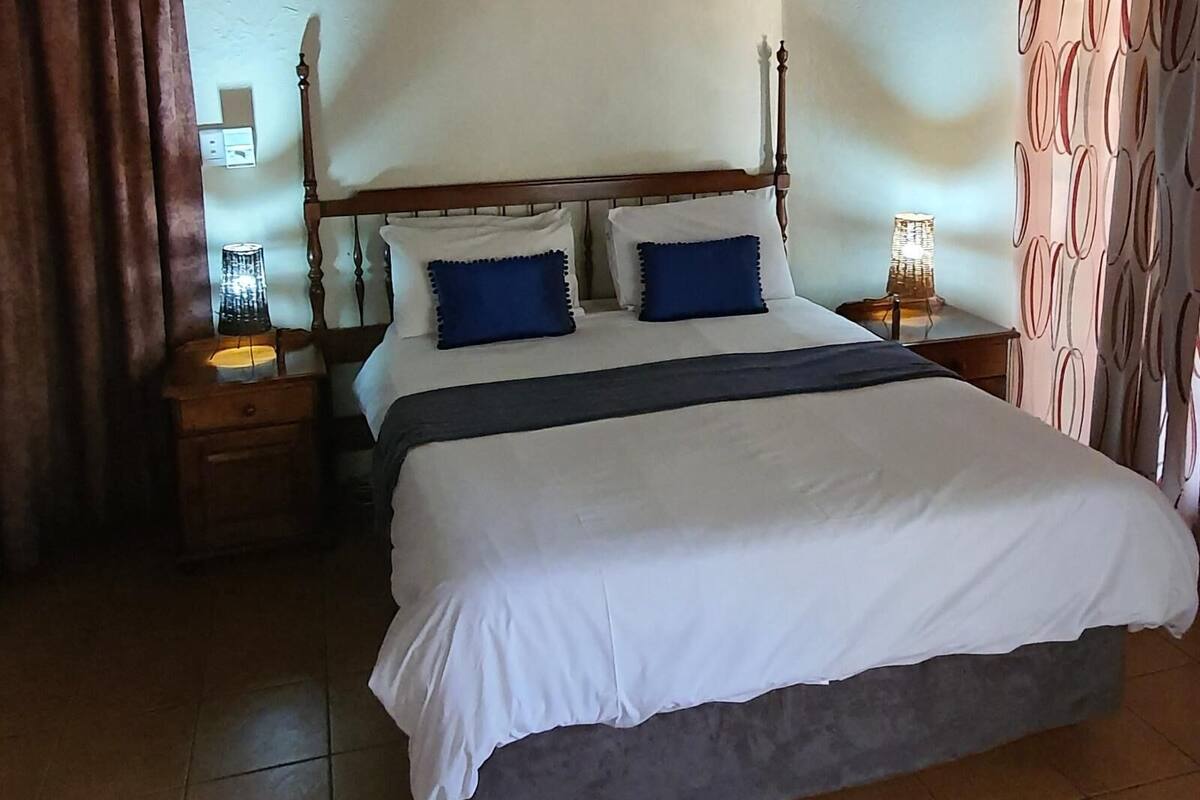 Una cama bien hecha con ropa de cama blanca y azul, un cabecero de madera y dos mesitas de noche con lámparas.