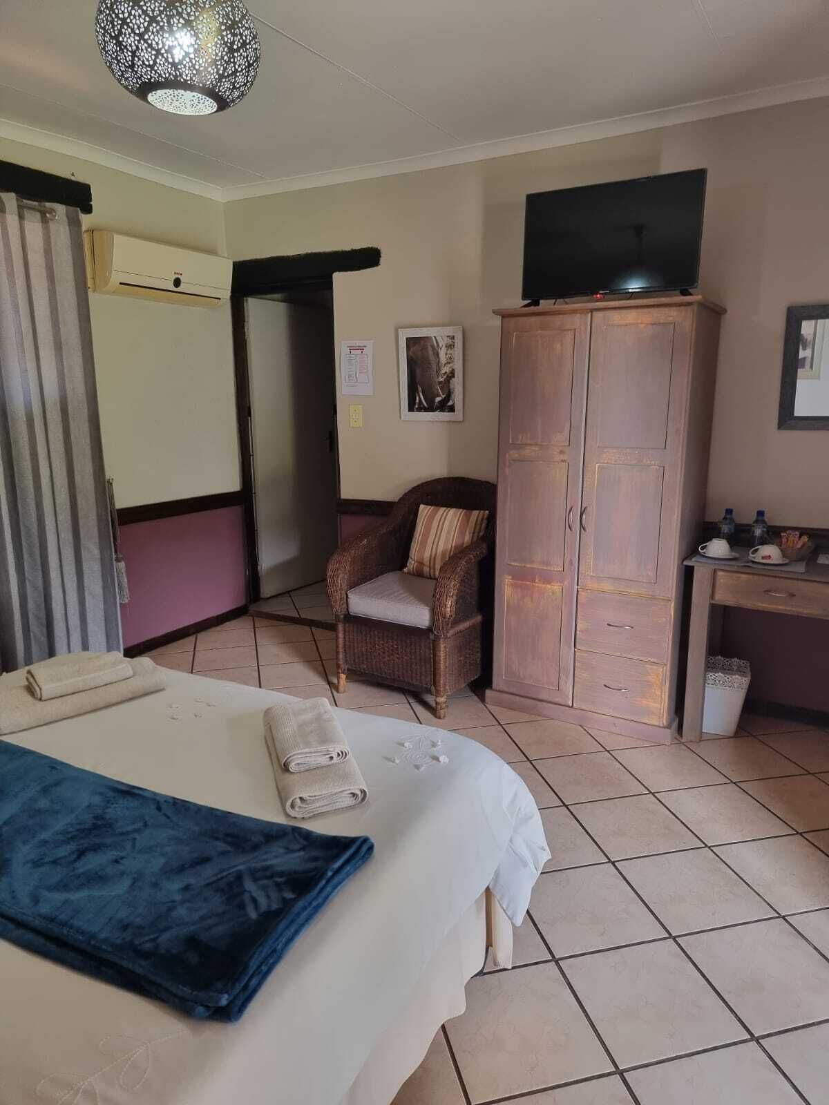A hotel room with a bed, a chair, a wardrobe, a desk, a television, and a trash bin.