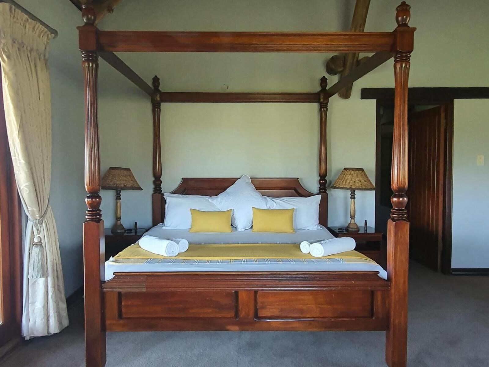 A four-poster bed with a wooden frame, white bedding, and two yellow pillows.