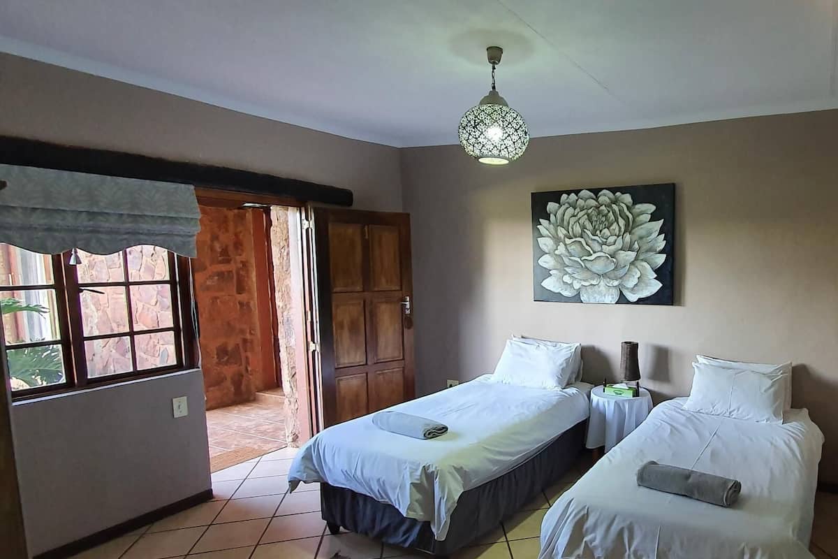 Una habitación con dos camas, una gran obra de arte floral en la pared, una lámpara colgante y vistas a través de una ventana con puerta de madera.