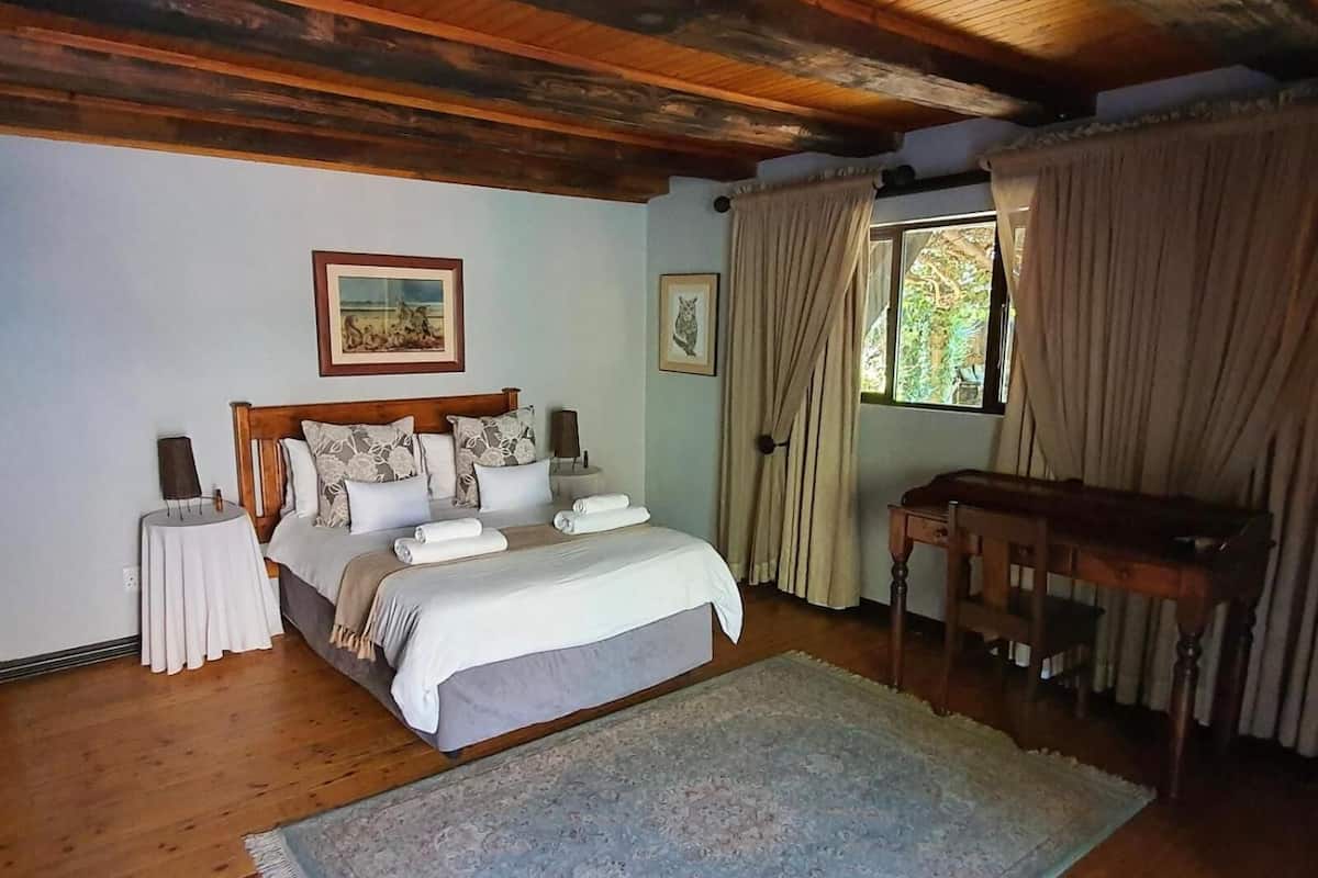 Un dormitorio con techo de madera, una cama con ropa de cama blanca, una mesita de noche, una mesa y una ventana con cortinas.